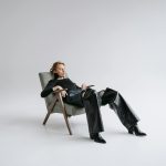 Stylish woman in black leather outfit reclines in a minimalist studio with open space.